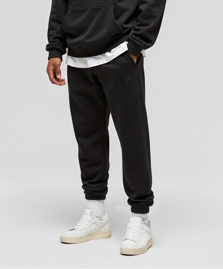 Person wearing a black hoodie and jogger set with white sneakers on a light gray background