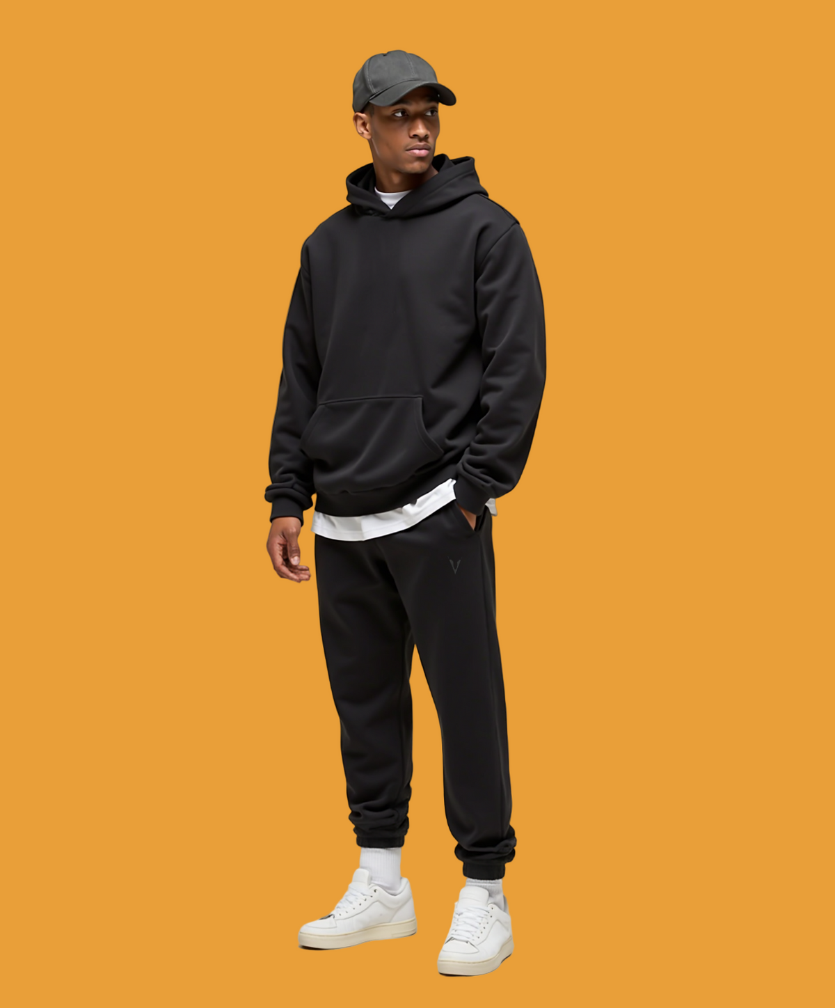 Person wearing a black hoodie and jogger set with white sneakers on a light gray background